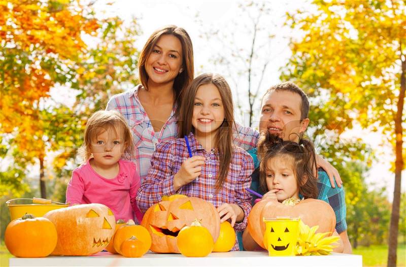 Mom dad and girls carving and draw scary pumpkins in the garden for Halloween party, stock photo