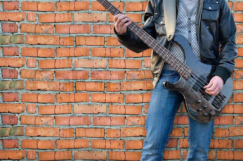 Man plays electric guitar on the background brick wall, stock photo