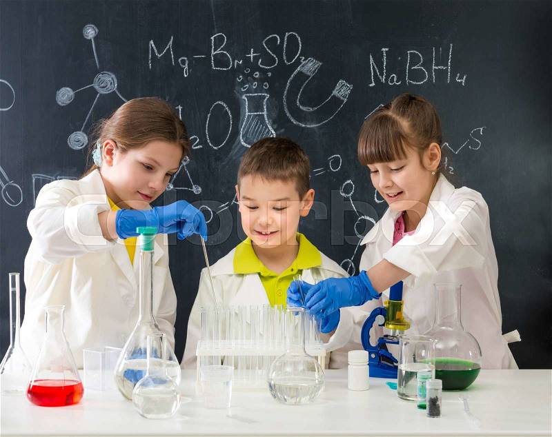 Three little students on chemistry lesson in lab doing an experiment, stock photo