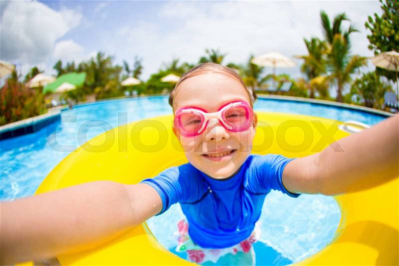 Little girl making selfie at inflatable rubber ring having fun in swimming pool, stock photo