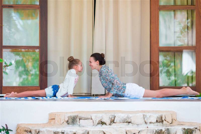 Mom and little girl doing yoga exercise outdoor on terrace, stock photo