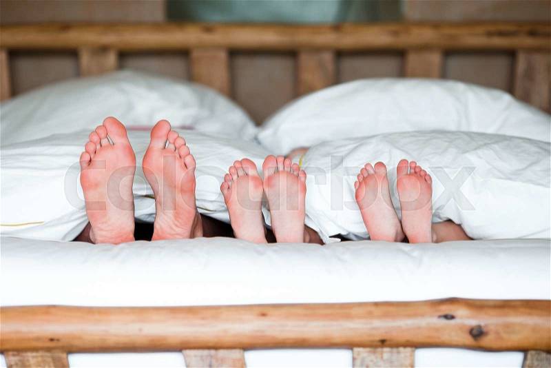 Family with two kids laying in bed with their feet forward, stock photo