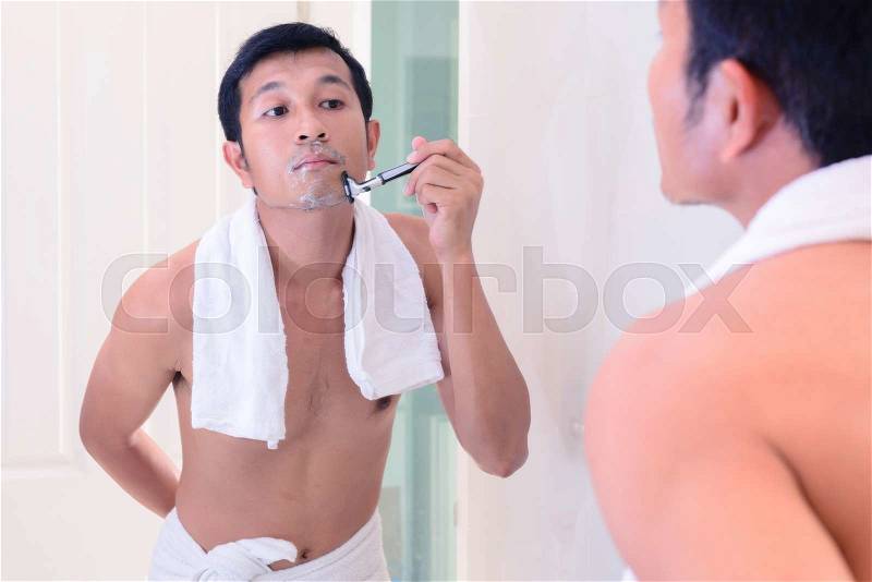 Young handsome man shaving by oneself with mirror, stock photo