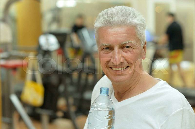 Elderly man in a gym. drinking water after exercise, stock photo