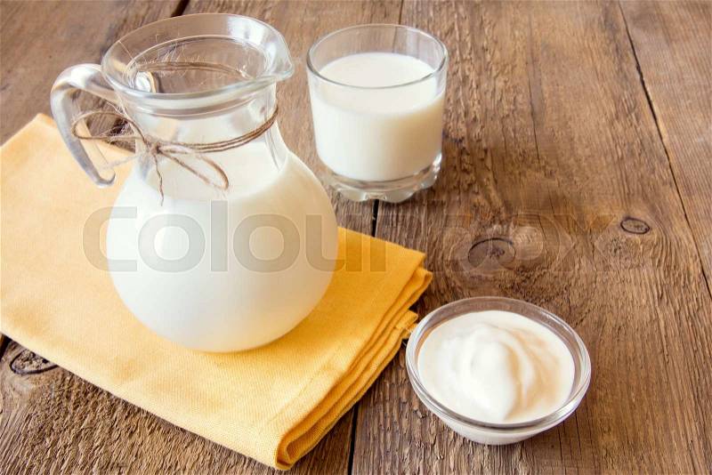 Calcium dairy fresh products: milk and sour cream (yogurt) on napkin and wooden table, close up, horizonal, copy space, stock photo