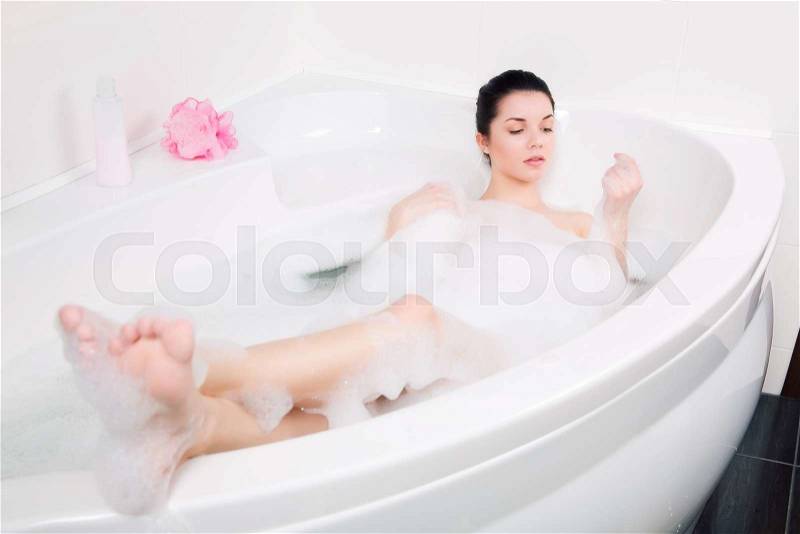 Young beautiful brunette woman takes bubble bath, stock photo