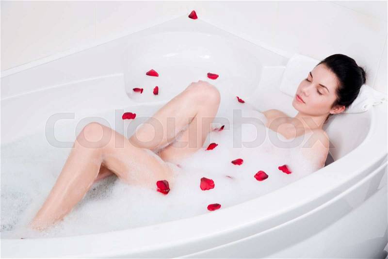 Beautiful young woman relaxing in bubble bath with rose petals, stock photo