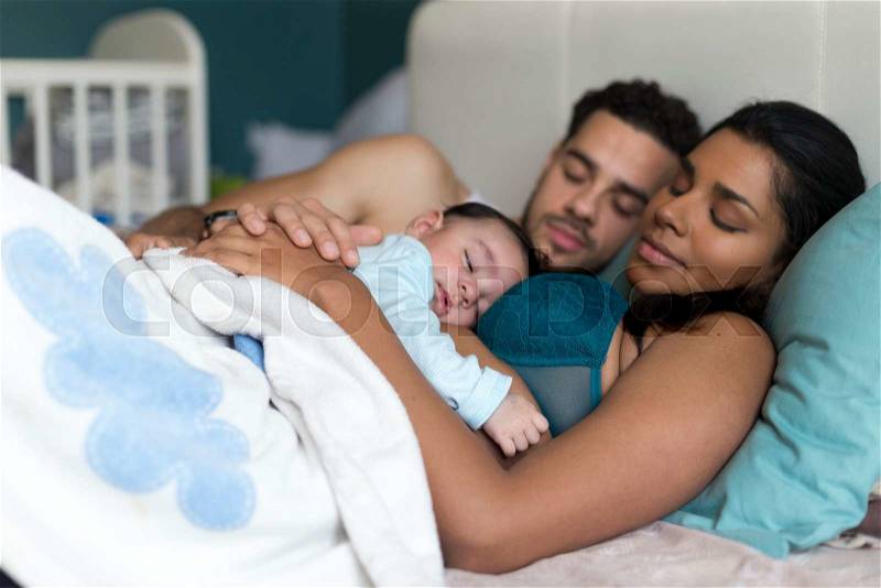 Young couple asleep in bed with their baby son sleeping on his mothers chest, stock photo