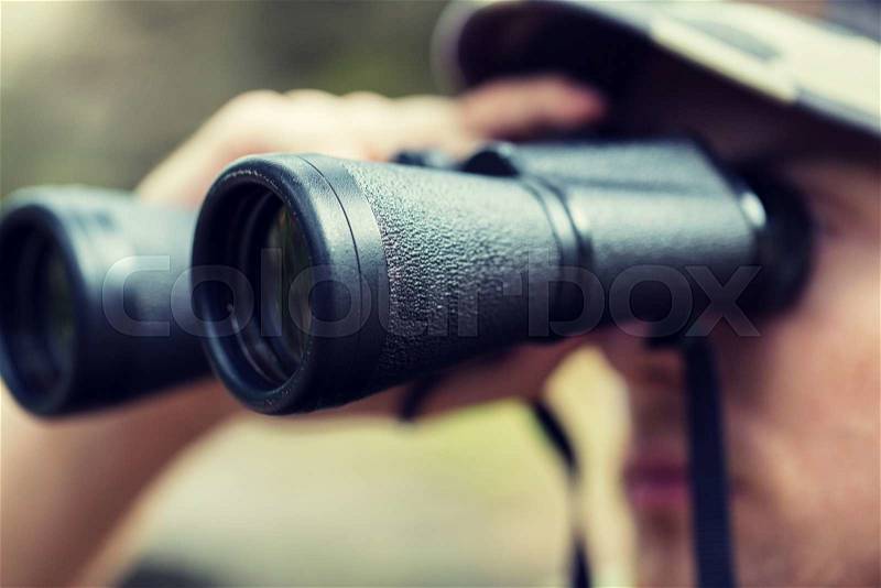 Hunting, war, army and people concept - close up of young soldier, ranger or hunter with binocular observing forest, stock photo