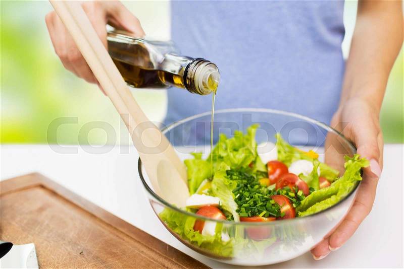 Healthy eating, vegetarian food, dieting and people concept - close up of young woman dressing vegetable salad with olive oil over green natural background, stock photo