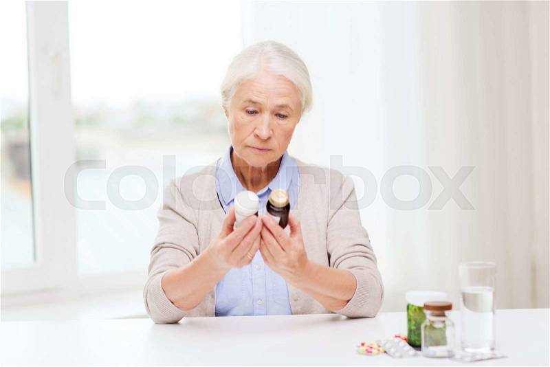 Age, medicine, health care and people concept - senior woman looking at jars with medicine at home or hospital office, stock photo