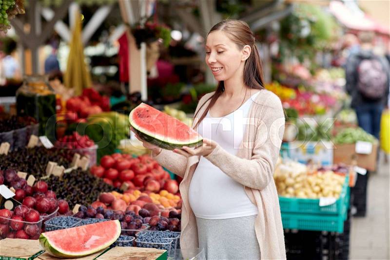 Sale, shopping, food, pregnancy and people concept - happy pregnant woman choosing watermelon at street market, stock photo