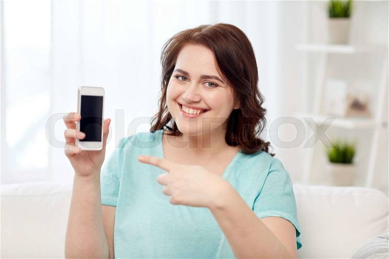 People, technology, communication and leisure concept - happy young plus size woman sitting on sofa and showing smartphone blank screen at home, stock photo