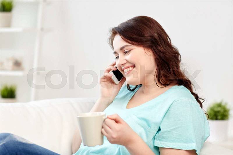 People, technology, communication and leisure concept - happy plus size young woman with cup of coffe or tea calling on smartphone at home, stock photo
