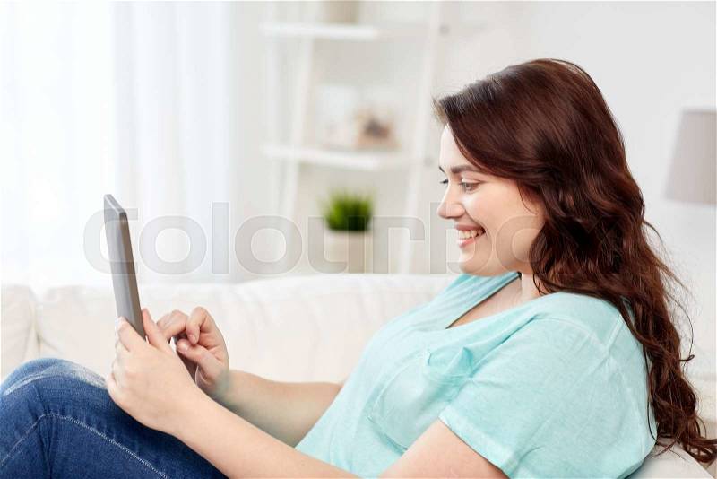 Technology, internet and people concept concept - smiling young plus size woman sitting on couch with tablet pc computer at home, stock photo
