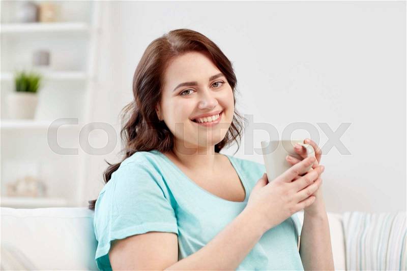 People, drinks and leisure concept - happy plus size young woman with cup of tea at home, stock photo
