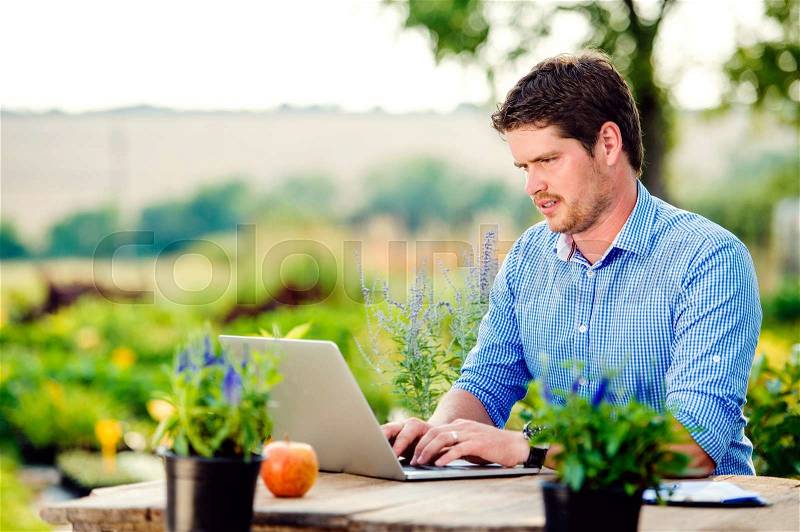 Gardener with notebook sitting at the table, managing supplies, green sunny nature, stock photo