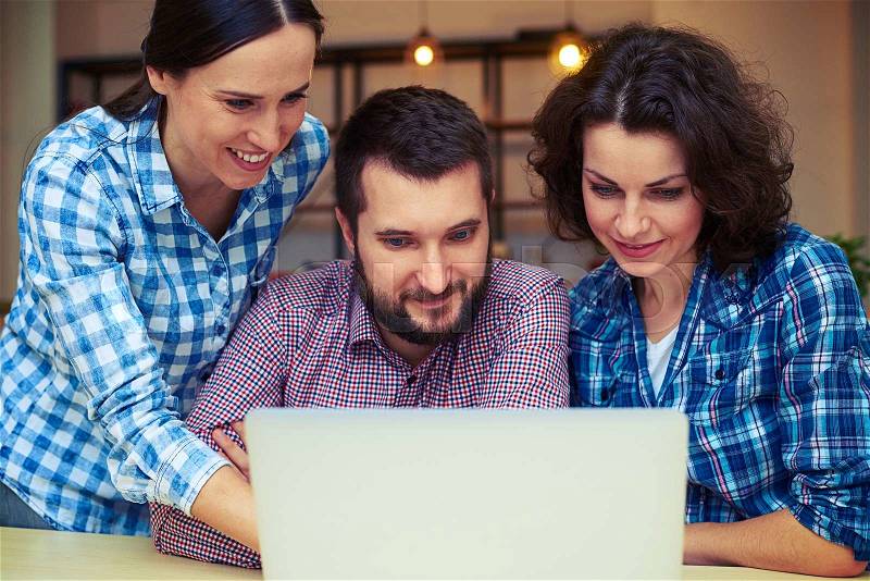 Cheerful team mates working with laptop in office, stock photo