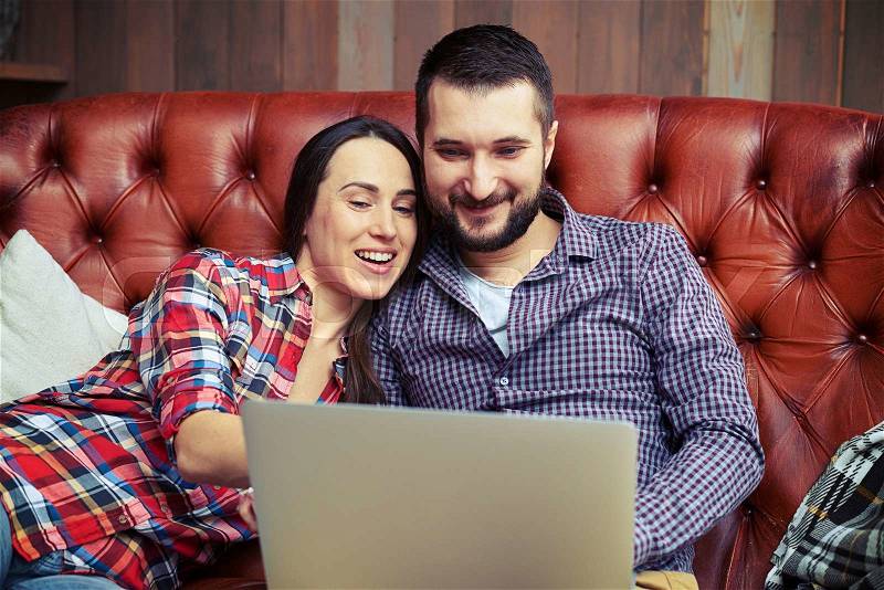 Smiley couple looking at laptop and browsing on internet, stock photo