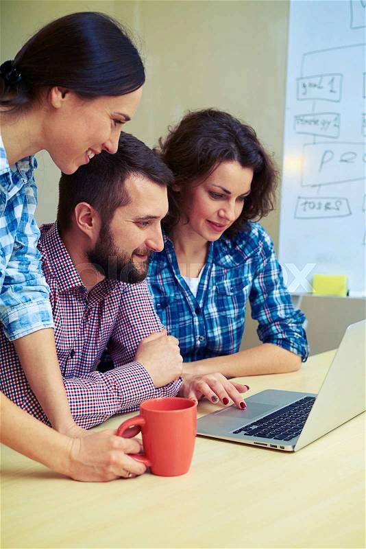 Three co-workers using laptop in office, stock photo