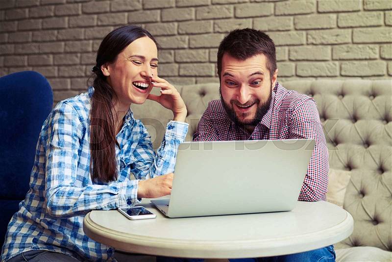Portrait of laughing couple looking at laptop at home, stock photo