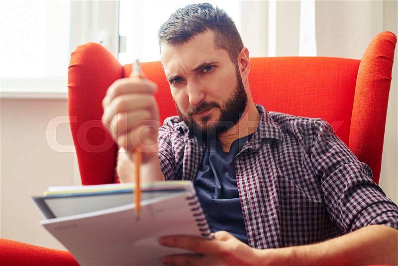 Young man sitting on the chair and making eye-measure with pencil, stock photo