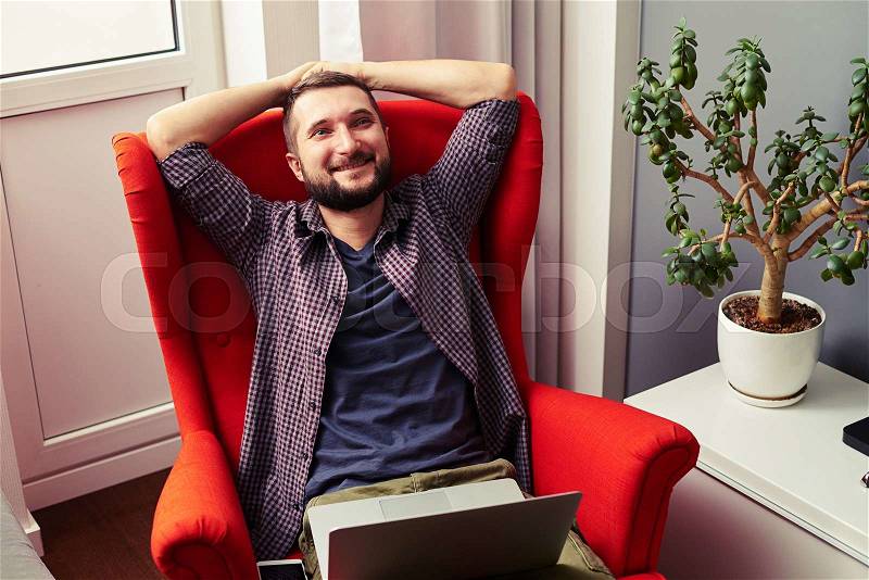 Smiley young man sitting on the chair with laptop and looking up, stock photo