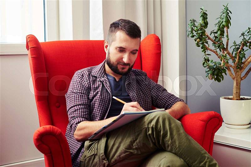 Young man sitting on the red chair and writing something, stock photo