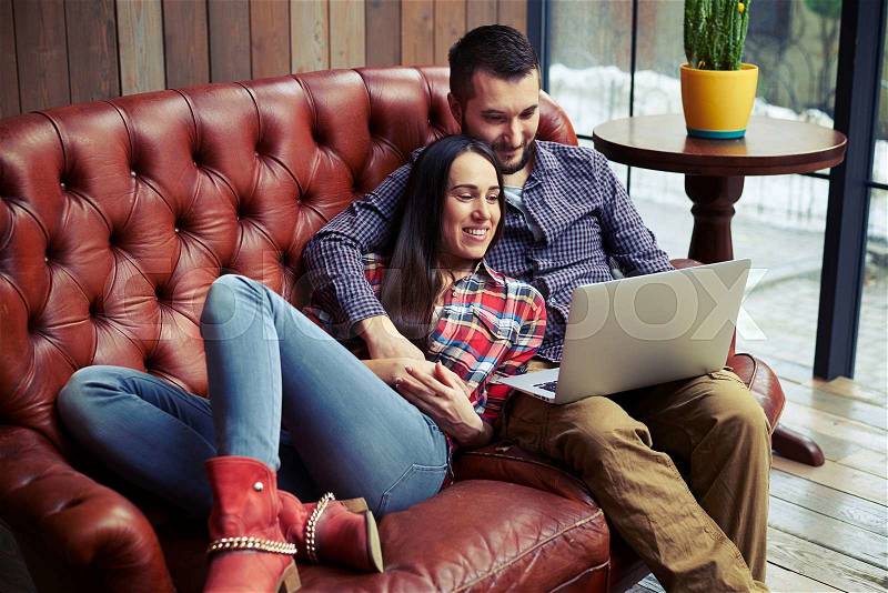 Smiley couple resting on sofa and looking at laptop, stock photo