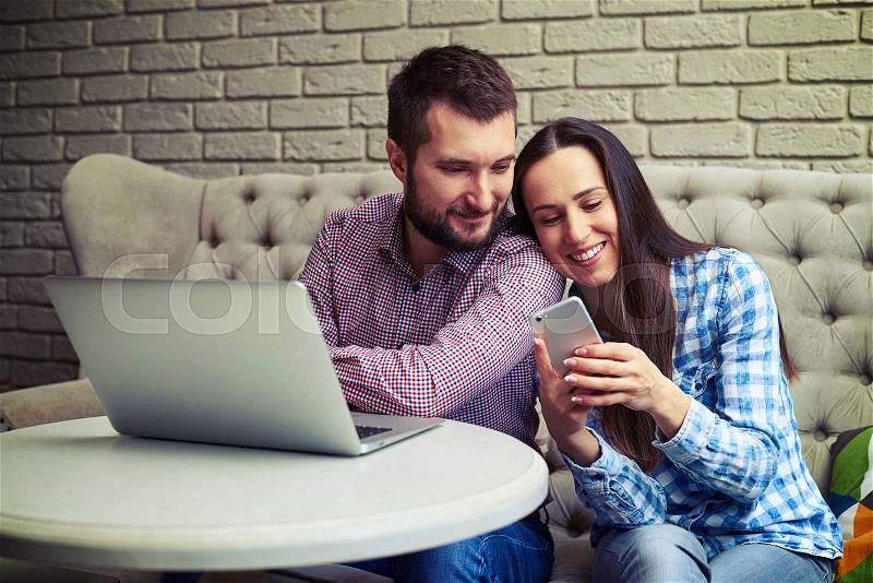 Smiley young couple sitting on sofa and using gadgets , stock photo