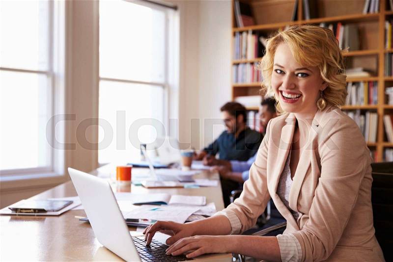 Businesswoman Using Laptop At Desk In Busy Office, stock photo