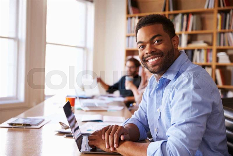 Businessman Using Laptop At Desk In Busy Office, stock photo