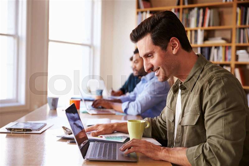 Businessman Using Laptop At Desk In Busy Office, stock photo