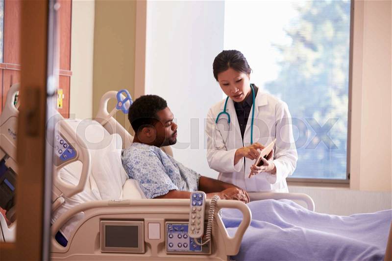 Hospital Doctor With Digital Tablet Talks To Male Patient, stock photo