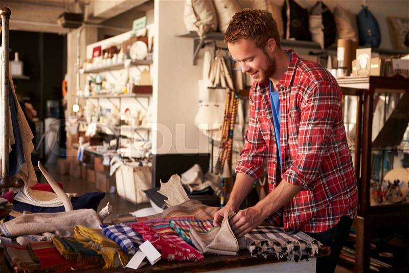 Male Sales Assistant Arranging Textiles In Homeware Store, stock photo