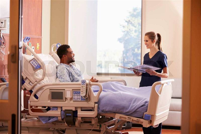 Female Doctor Talking To Male Patient In Hospital Bed, stock photo