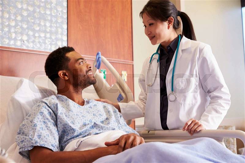 Female Doctor Talking To Male Patient In Hospital Bed, stock photo