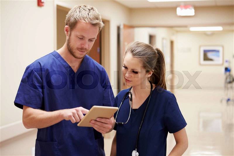 Medical Staff Looking At Digital Tablet In Hospital Corridor, stock photo