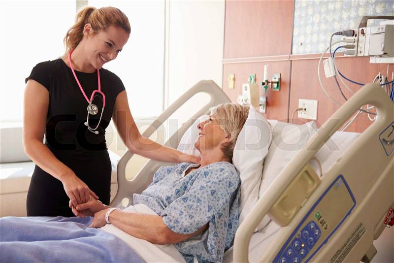 Female Doctor Talks To Senior Female Patient In Hospital Bed, stock photo