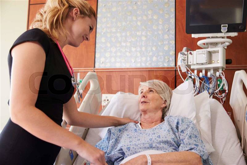 Female Doctor Talks To Senior Female Patient In Hospital Bed, stock photo