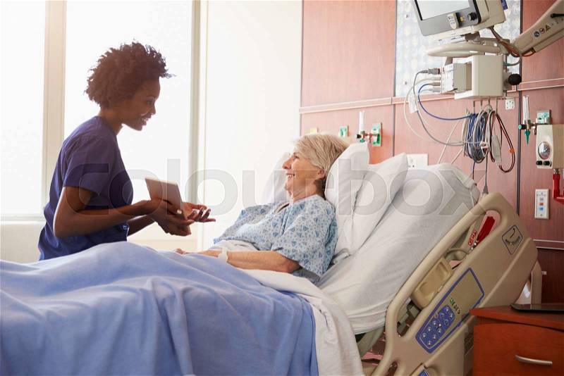 Hospital Nurse With Digital Tablet Talks To Senior Patient, stock photo