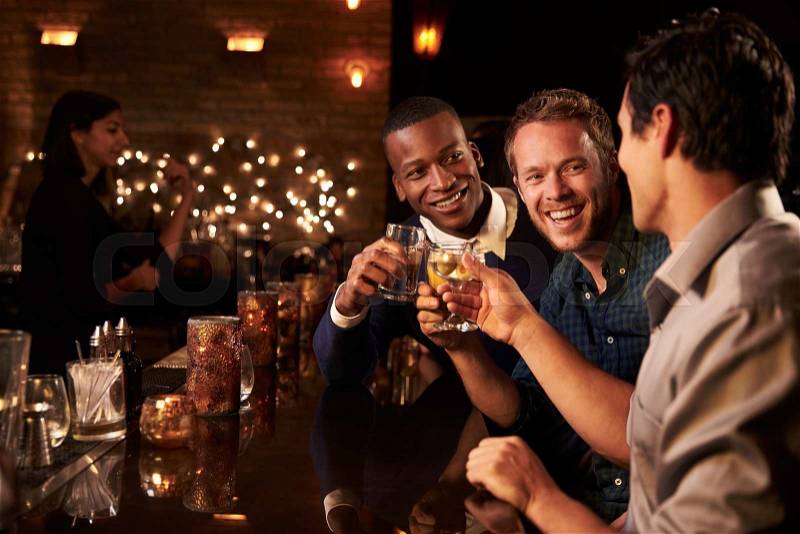 Male Friends Enjoying Night Out At Cocktail Bar, stock photo