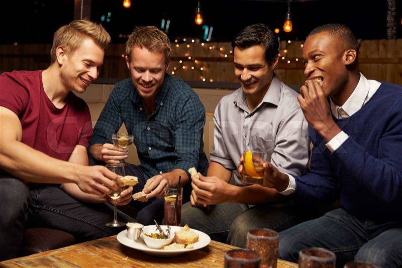 Group Of Male Friends Enjoying Night Out At Rooftop Bar, stock photo