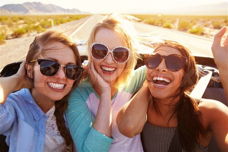 Three Female Friends On Road Trip In Back Of Convertible Car, stock photo