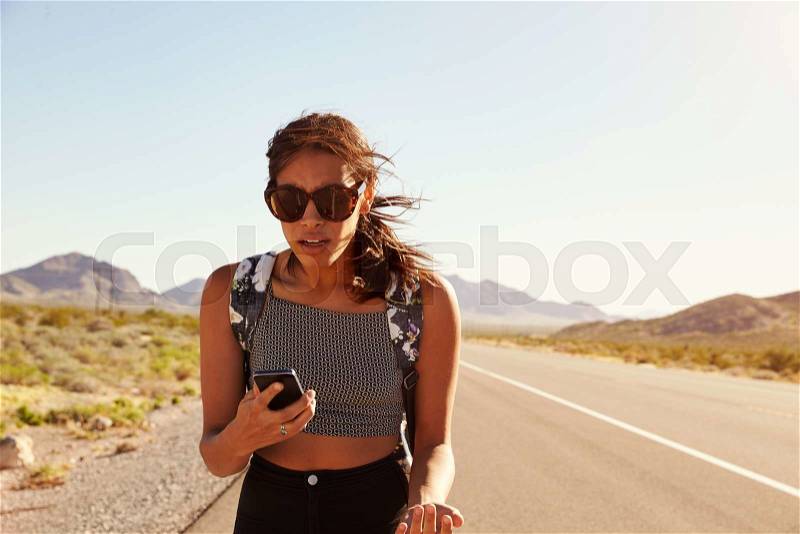 Woman On Vacation Hitchhiking Along Road Using Mobile Phone, stock photo