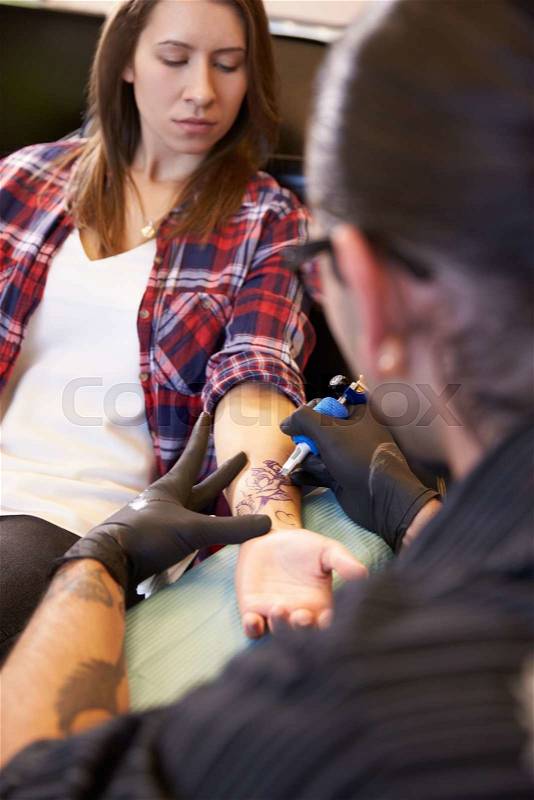 Woman Sitting In Chair Having Tattoo On Arm In Parlor, stock photo