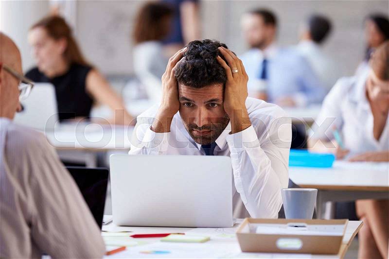 Stressed Businessman Working On Laptop In Busy Office, stock photo
