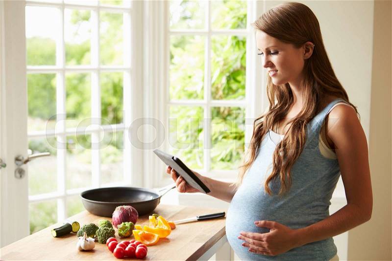 Pregnant Woman Following Recipe On Digital Tablet, stock photo