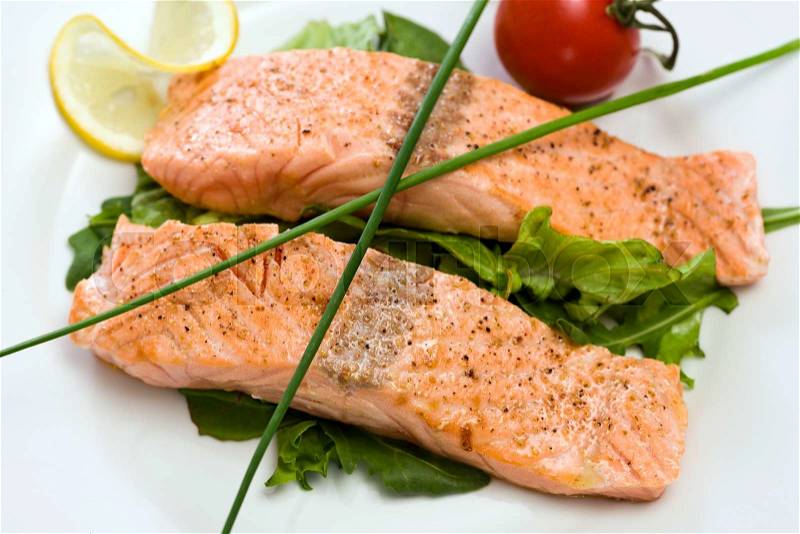 Two fried salmon fillets close-up, garnished with chives, lemon slice, tomato, on a bed of green salad, stock photo