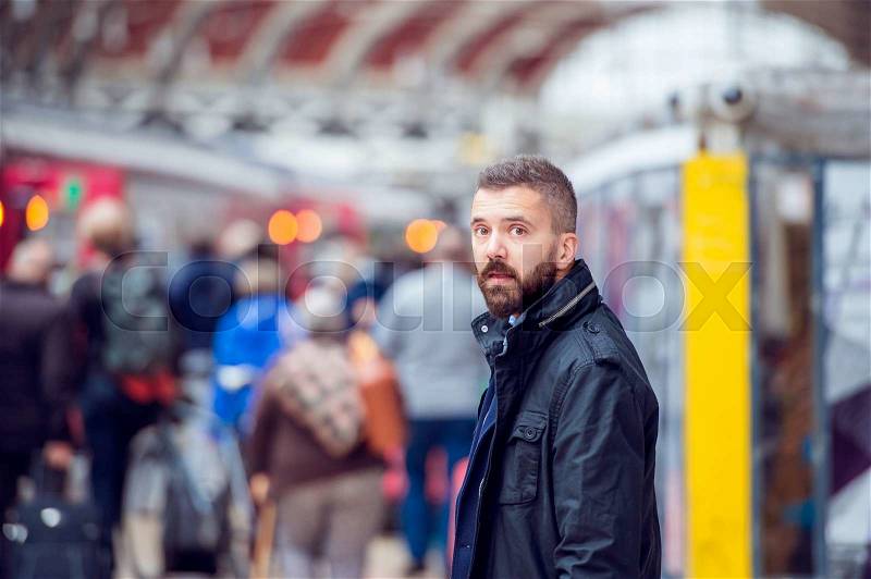Young handsome hipster man in black jacket waiting at the crowded train station, stock photo